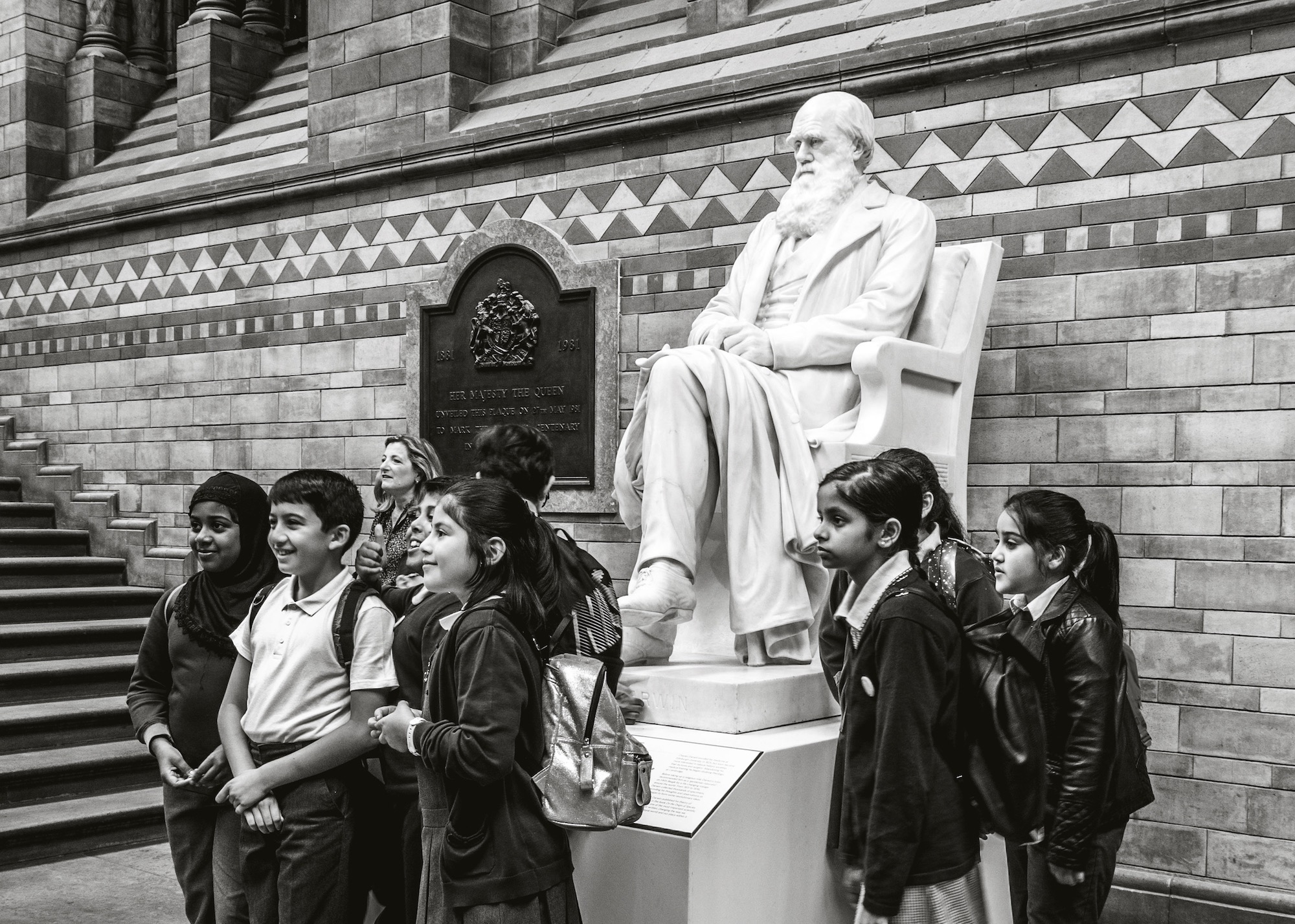 Schoolchildren on a school trip, posing for a photograph in front of the Charles Darwin statue, at the Natural History Museum, London, England, UK.
