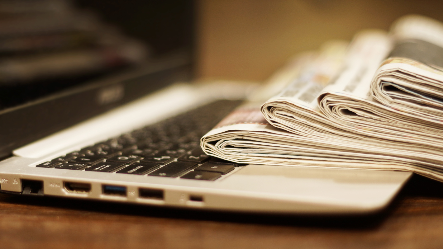 A laptop with folded newspaper resting on the keyboard