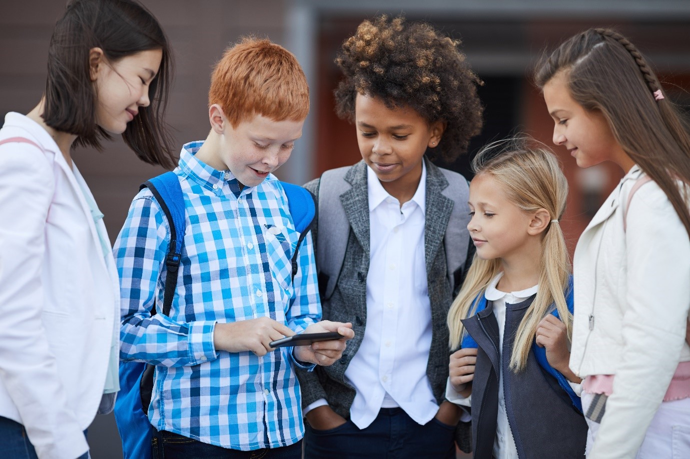 A group of four children crowd round a child with a mobile phone and look at the screen