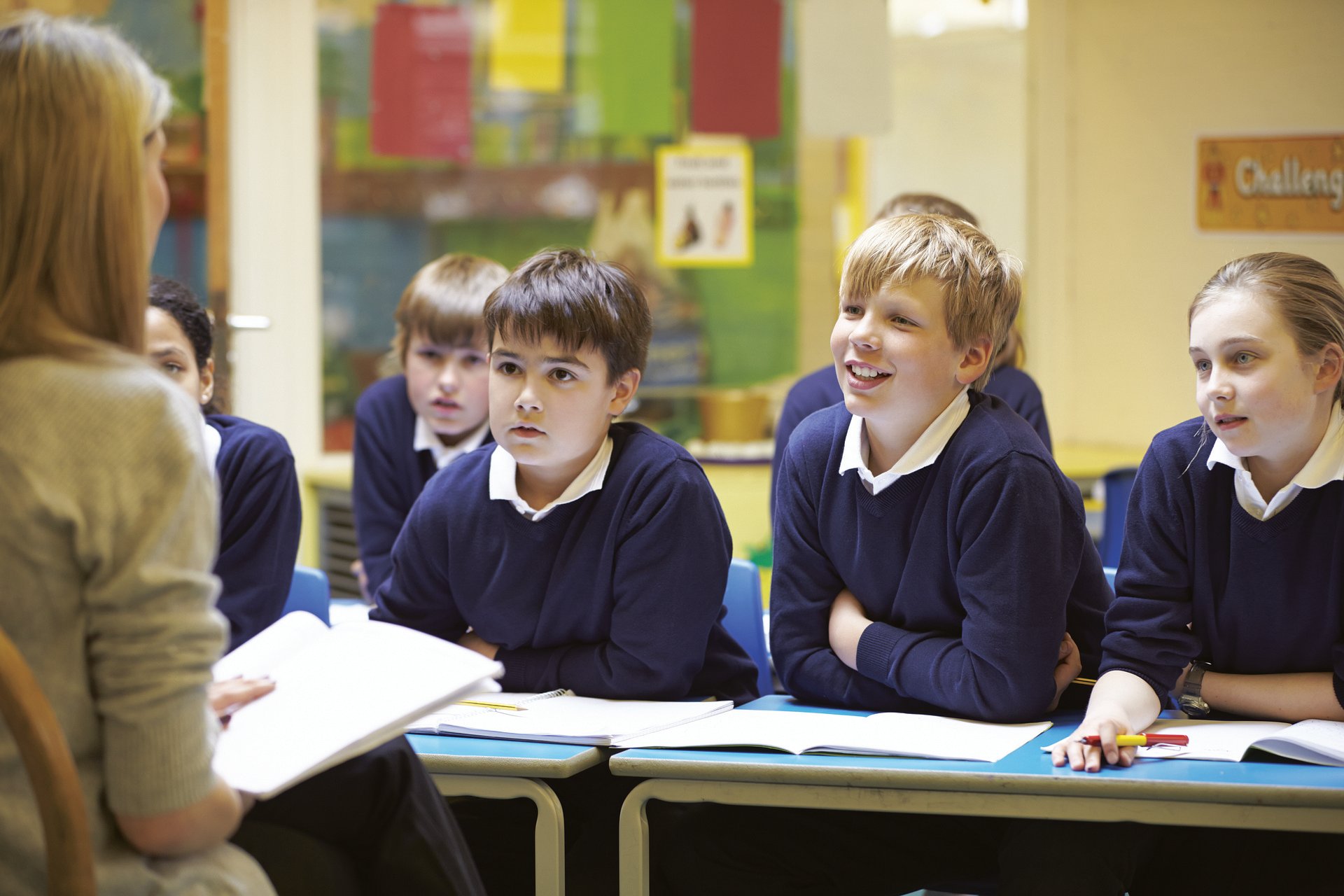 School children in a classroom listening to their teacher read a book