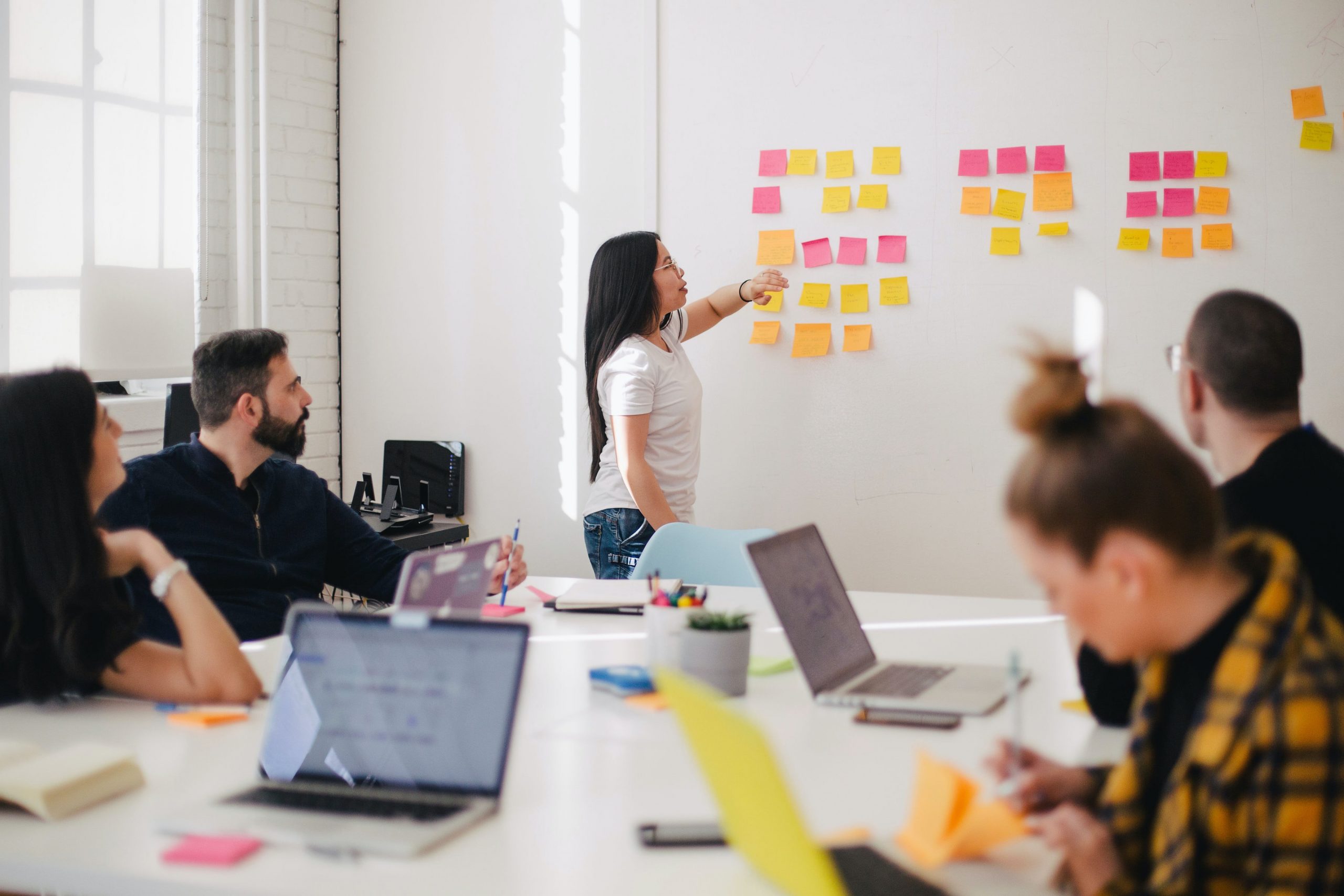 A group session in a meeting room where the group leader is moving around post-it notes on a whiteboard.